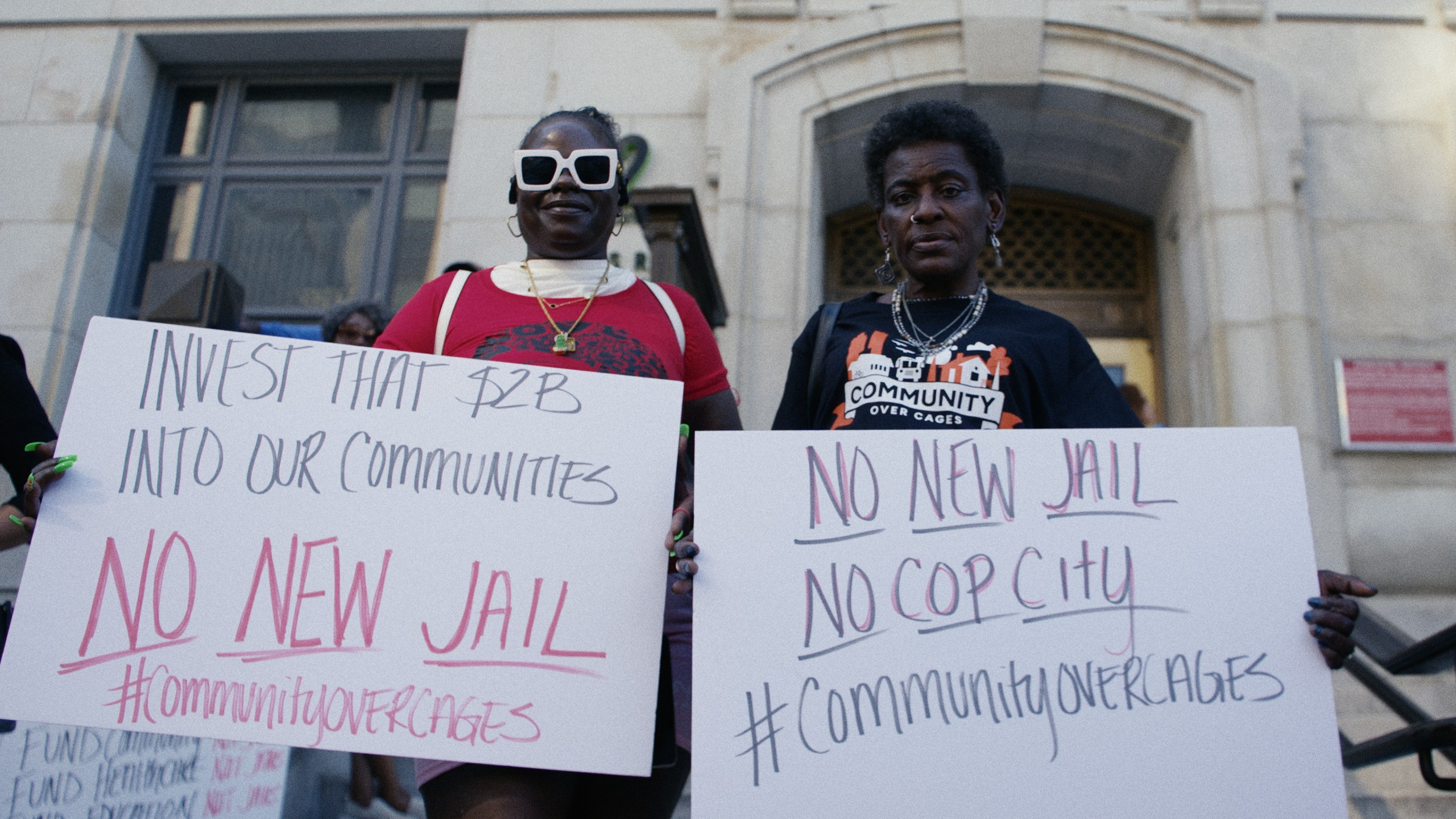 Two advocates, both Black women, hold signs outside the Fulton County Courthouse. (Atlanta Community Press Collective)