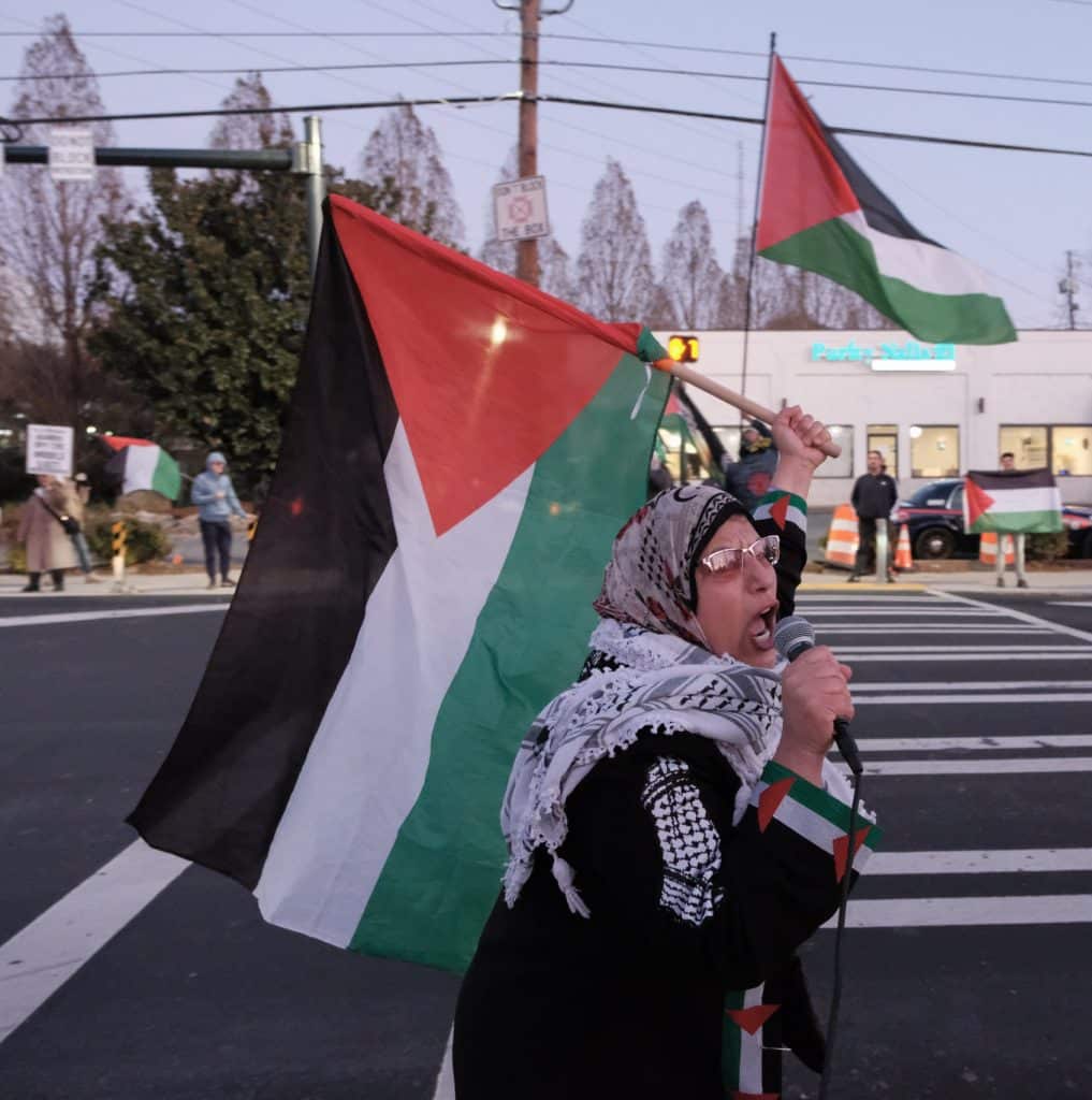 Jawahir, an organizer in Atlanta, carries a Palestinian flag and chants into a microphone as she rallies the crowd at the International Day of Solidarity Protest.