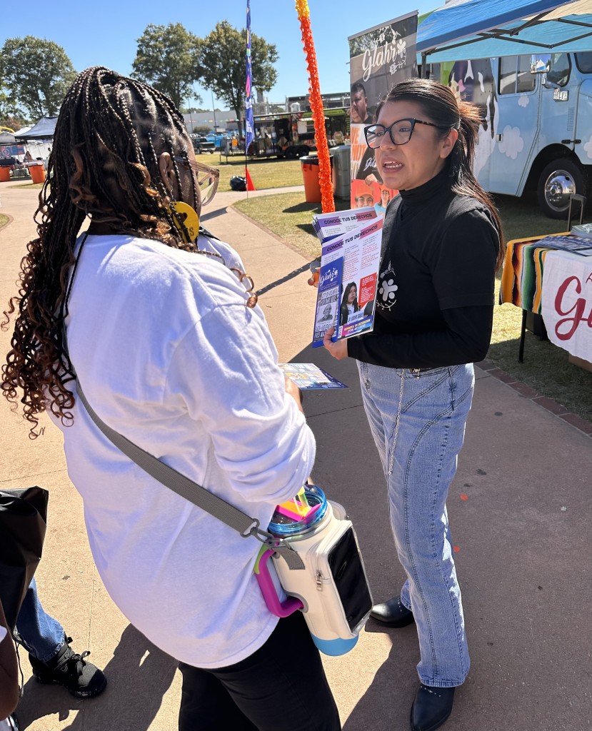 Foreground: A community member stands listening to Annette Aguilar, a GLAHR organizer holding a "Know Your Rights" flyer. GLAHR organizes ICE Chasers.