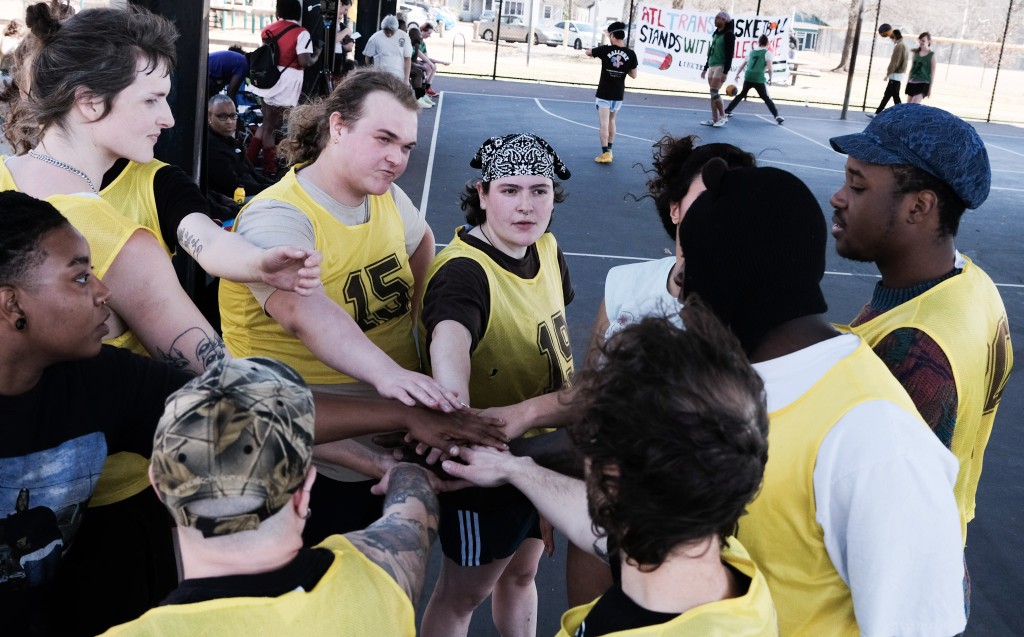 Basketball players wearing yellow stand in a circle and extend their hands into the middle for a team chant.