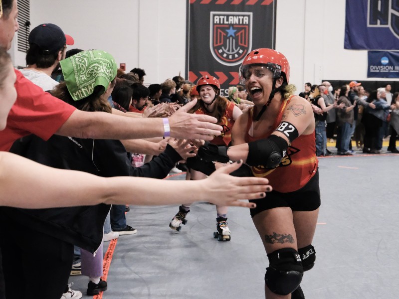A roller derby player smiles while skating and giving high fives to fans.
