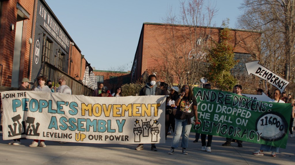 Protesters standing outside of Monday Night Garage in West End holding signs that say, "Join the People's Movement Assembly" and "Andre Dickens, you have dropped the ball on democracy."