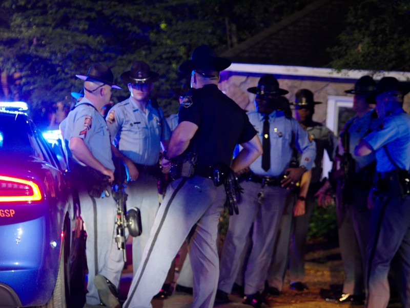 A group of Georgia State Troopers stand beside a Georgia State Patrol vehicle at night