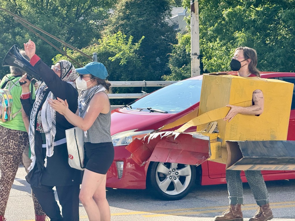 A protester wearing a homemade bulldozer costume dances on a bridge in Atlanta to protest the Cop City ribbon-cutting.